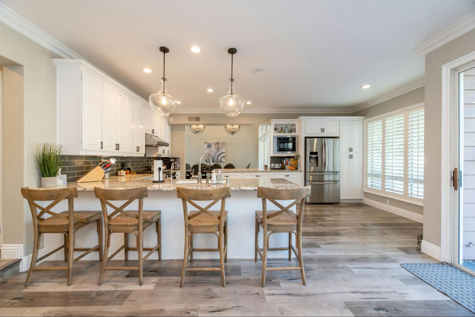 A bright modern kitchen featuring white cabinetry, rustic wood bar stools and stainless steel appliances. Open, stylish and functional with warm natural light