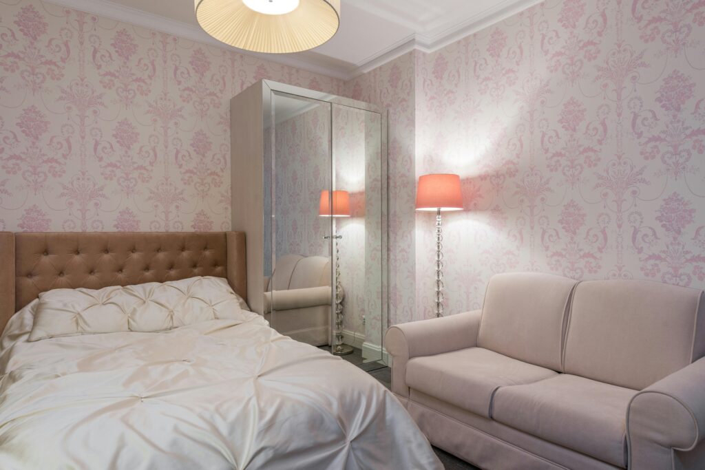 A cosy pink-themed bedroom featuring a tufted bed, pastel sofa, mirror wardrobe, and warm ambient lighting for a soft, elegant atmosphere